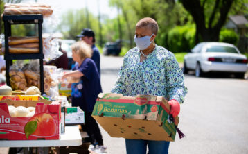 Photo of a woman carrying food donations while wearing a mask.